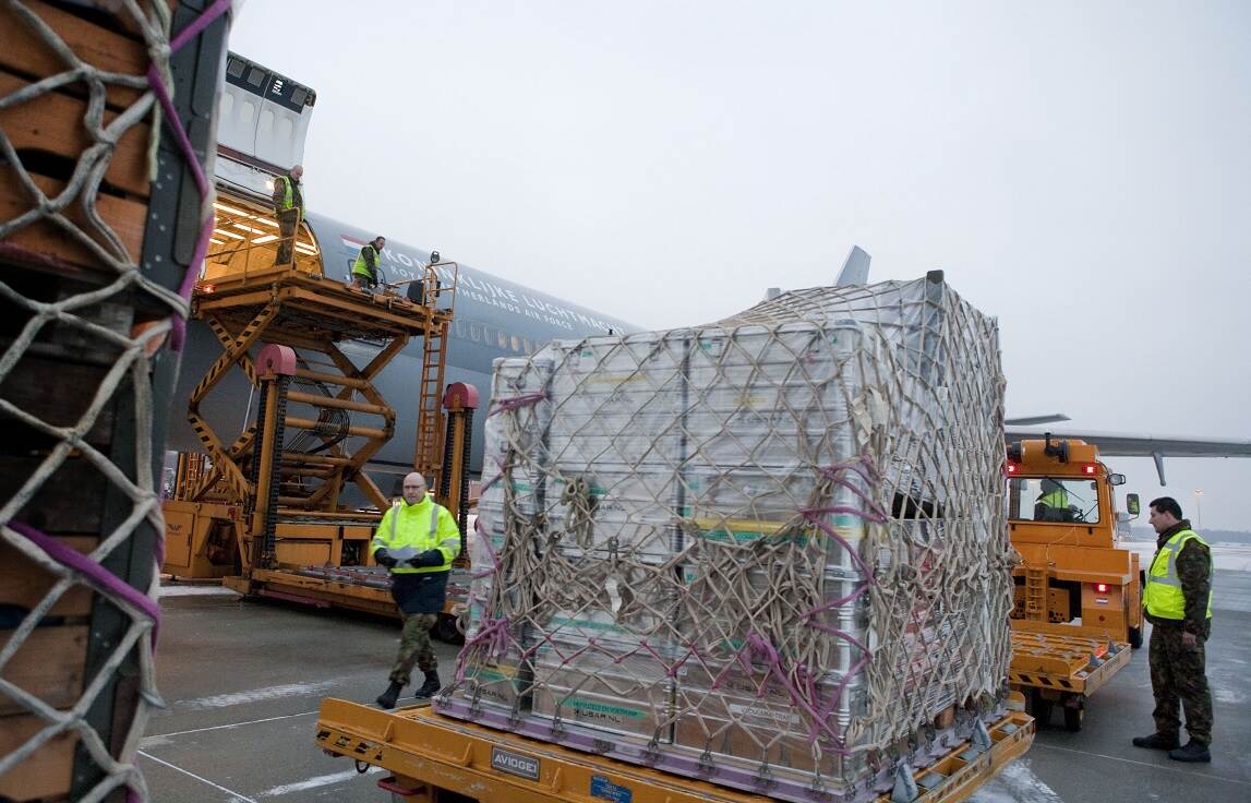Militairen laden op een vliegveld goederen in een vliegtuig van de Koninklijke Luchtmacht. In beeld zijn kratten met goederen omwikkeld met netten.