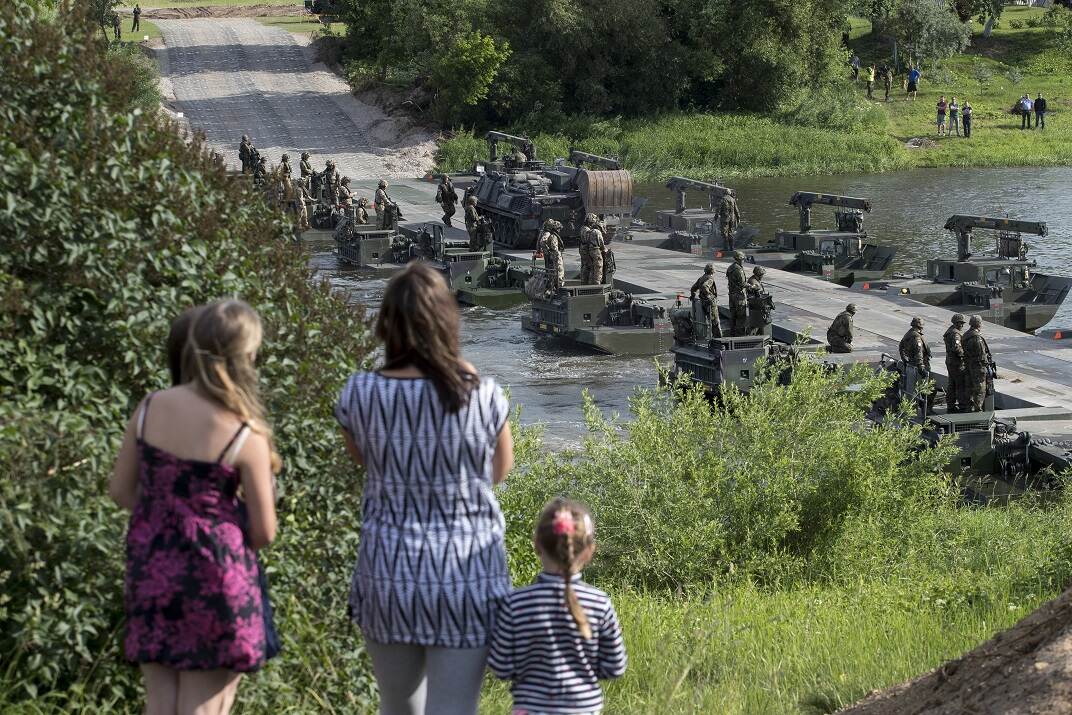 Inwoners Litouwen kijken tijdens een oefening van Nederlandse militairen hoe de militairen een brug bouwen over de rivier.